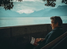 man sitting while holding a book watching on body of water